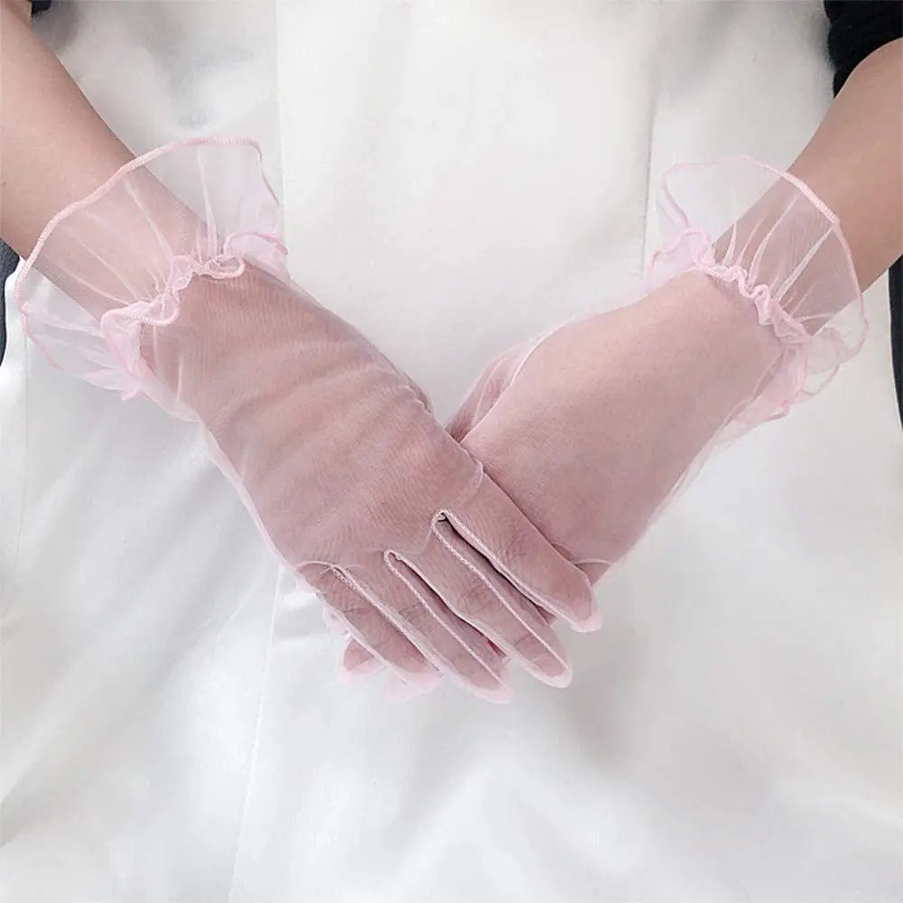 Duas mãos cruzadas com luvas transparentes rosa-pálido diante de um vestido branco