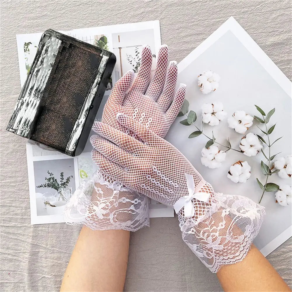 Weiße Netzhandschuhe mit Spitzenmanschetten und kleinen Schleifen neben Baumwollblüten
