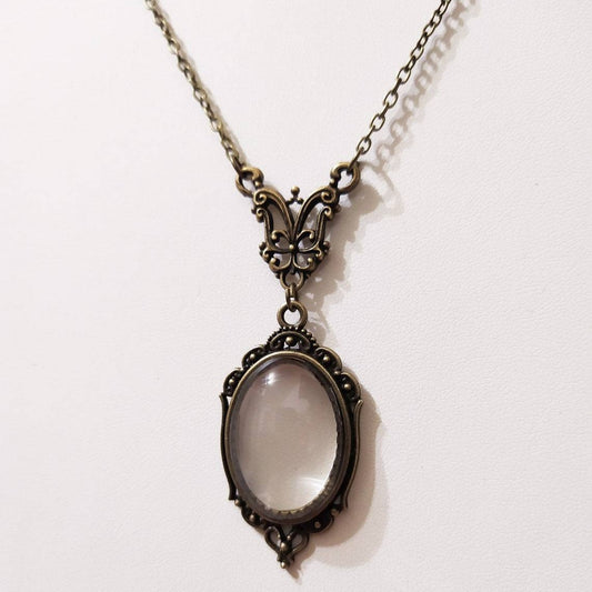 Octavia — lupa ovalada y cadena en tono bronce sobre fondo claro
